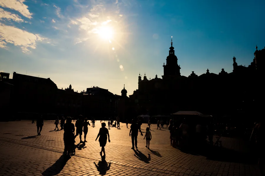 Silhouetted figures crossing a sunlit old town square in Krakow, Poland at golden hour